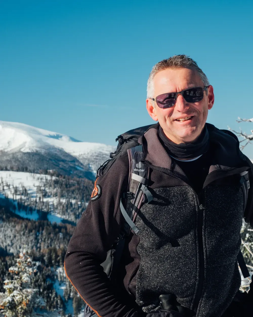 Andreas Kohlbacher lächelnd auf einer Winterwanderung, verschneite Berge im Hintergrund