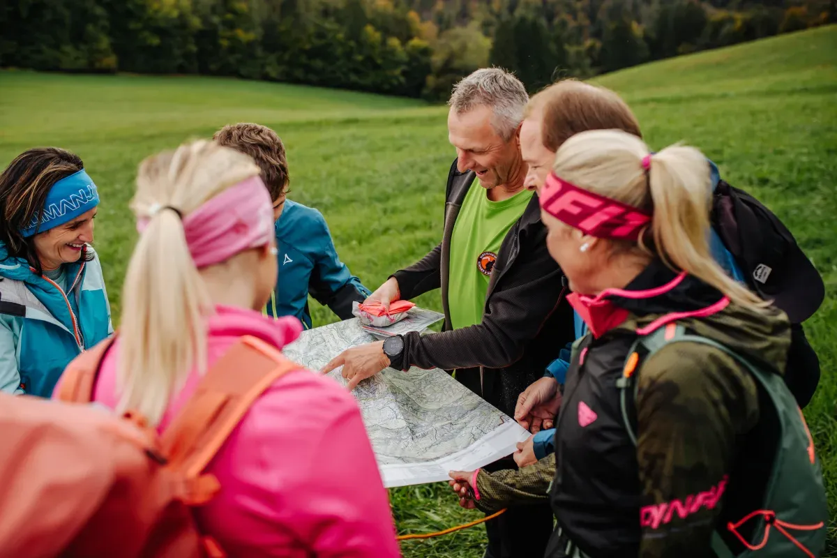 Wandergruppe liest gemeinsam eine topografische Wanderkarte auf einer Wiese